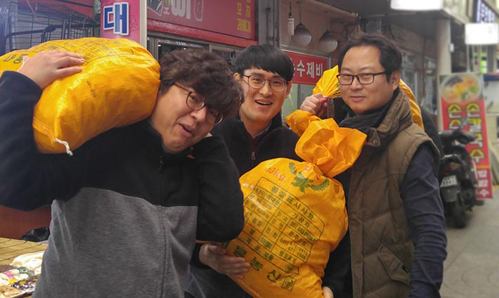 사람3명이 재래시장에서 구매한 농수산물을 짊어지고 카메라를 보며 찍은 사진